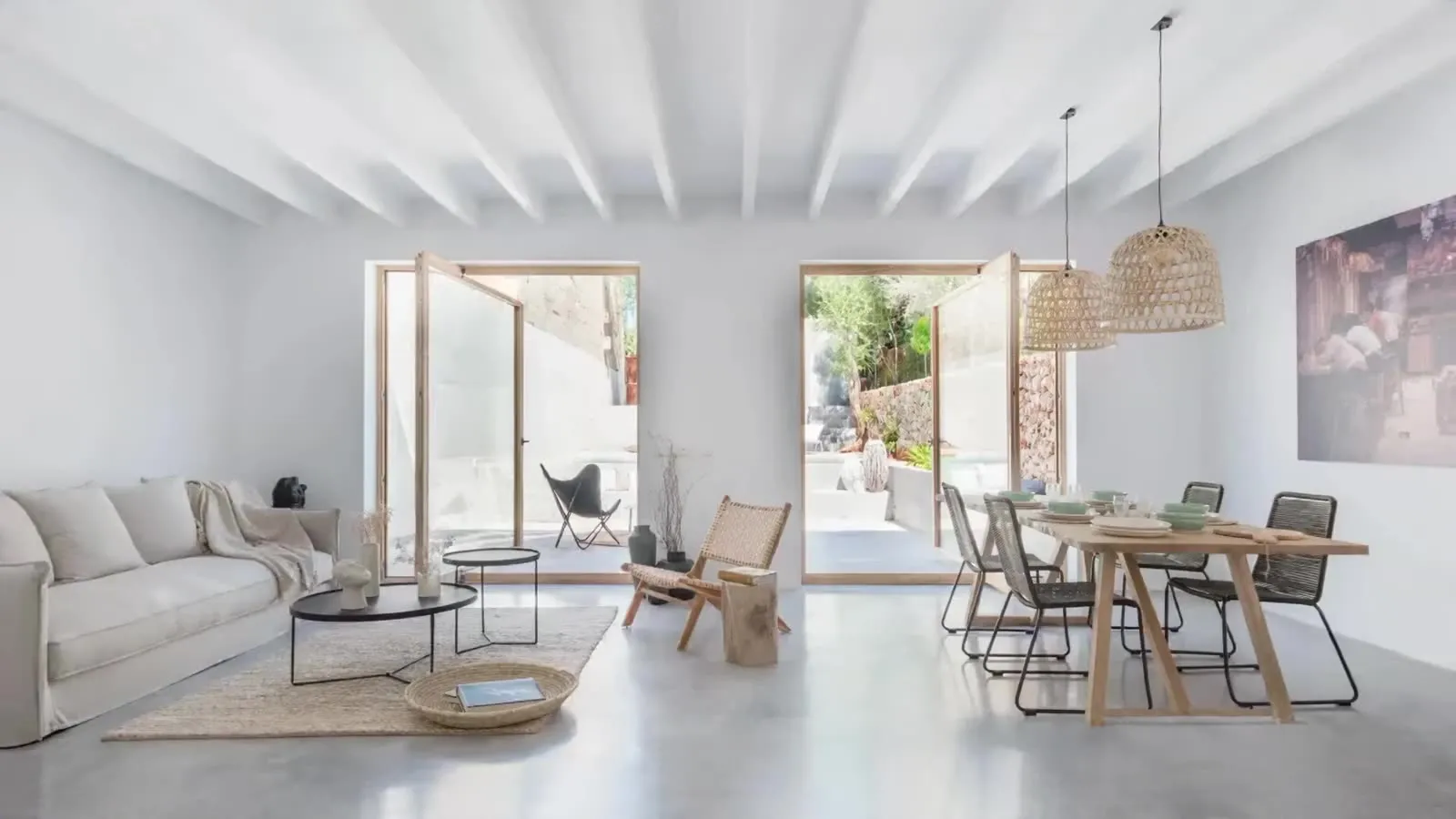Salón comedor de una vivienda reformada llave en mano por Stylo 10, con vigas blancas, suelo continuo y las puertas abiertas al patio