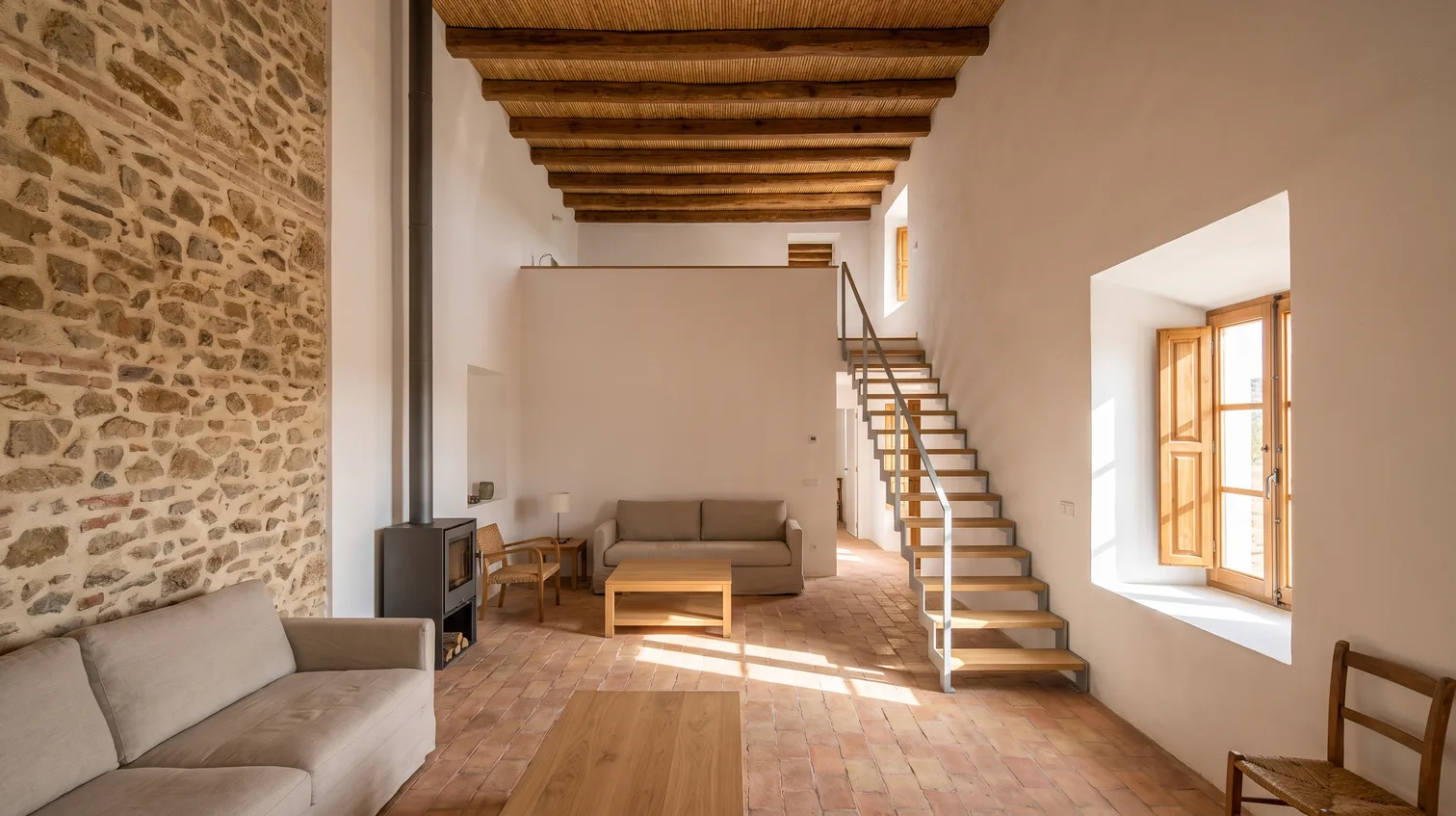 Salón a doble altura de una casa de pueblo rehabilitada en el Alto Guadalquivir, con muro de mampostería consolidado, forjado de rollizos y escalera de acero y roble