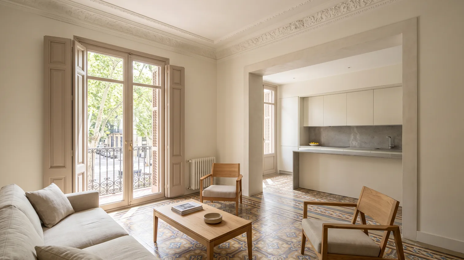 Salón de una vivienda del ensanche de Córdoba tras la reforma, con molduras de escayola restauradas, mosaico hidráulico original y cocina abierta al fondo