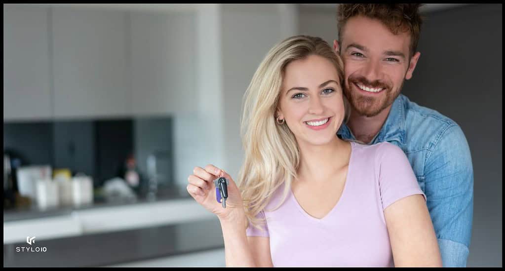 Una pareja joven sonríe mientras sostiene las llaves de su nueva casa en una cocina moderna. La imagen simboliza la felicidad y el logro de adquirir una nueva propiedad